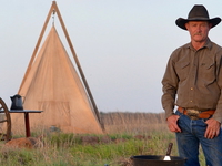 Kent Rollins stands next to a cast-iron grill and a tent.